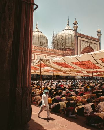 Man walking beside men praying in Jama Masjid in Delhi, India