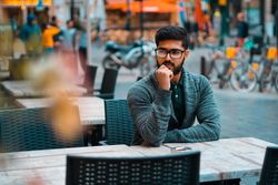 Man in gray sweater wearing framed eyeglasses sitting  outdoor