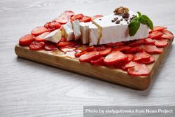 Large slice of cheese and sliced strawberries on wooden board bDgep4