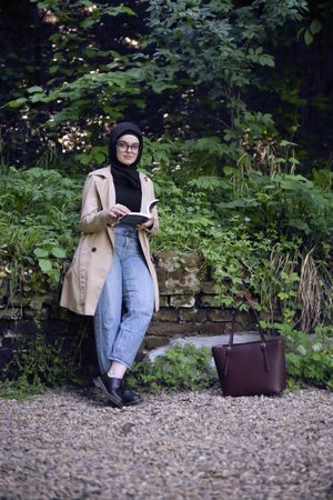 Serious Middle Eastern woman with book standing in a park