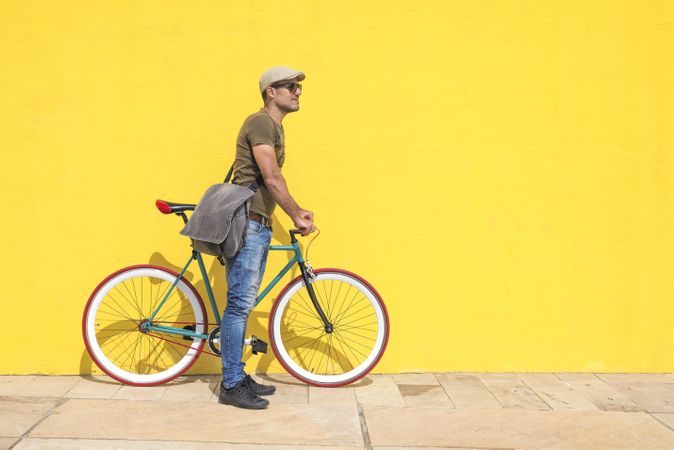 Man standing on bike next to yellow wall