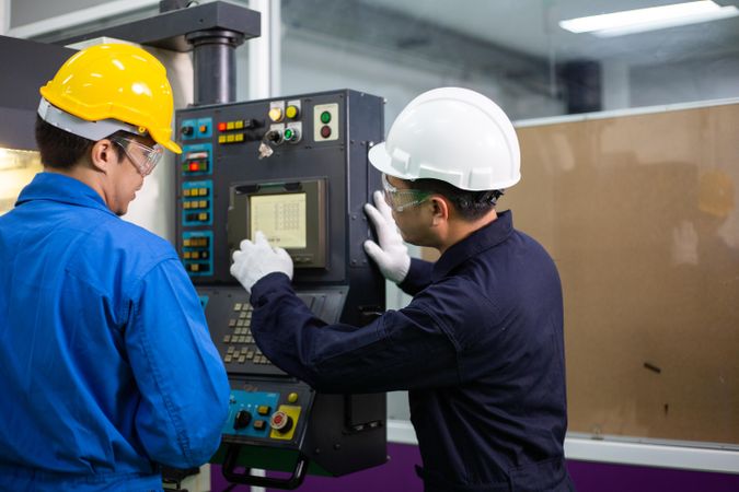 Two men in PPE gear operating controller in plant