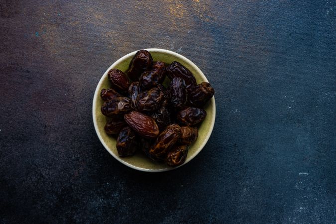Top view of organic dates in a yellow bowl on dark table