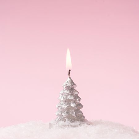 Silver Christmas tree lit candle with snow on pink background