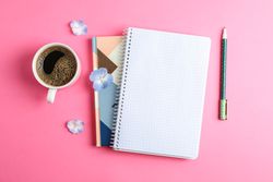 Cup of coffee with petals of flower, copybooks and pen on color background, top view