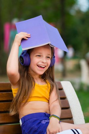 Preteen girl with book on bench in park