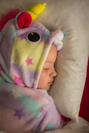 Girl in unicorn pajama sleeping in bed