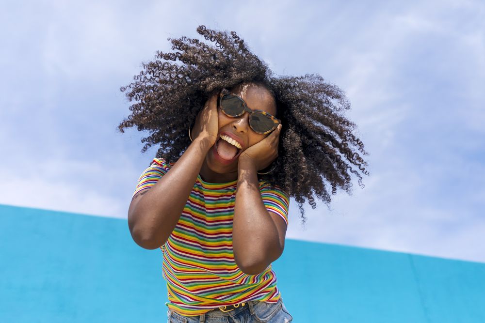 Portrait of beautiful Black woman with hands on her face while smiling and looking at camera against sky