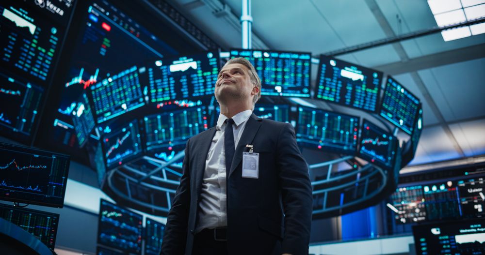 Stock Market Day Trader Working at an Exchange Office with Multi-Monitor Setup with Real Time Investment, Commodities and Foreign Funds Charts.