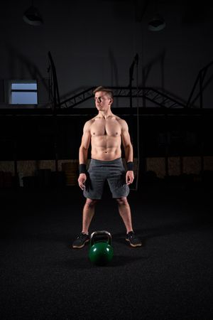 Muscular athlete with kettlebell in darkness
