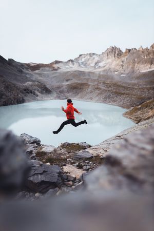 Side view of a man in red jacket jumping beside frozen lake in the mountain in Switzerland