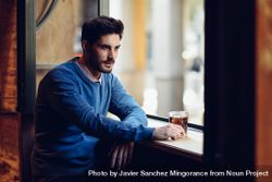 Man with blue sweater sitting with a drink in a modern pub 4OgDv4