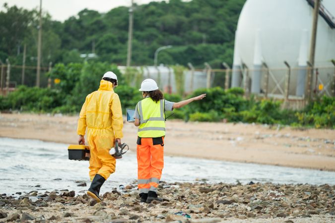 Workers in safety gear walking to survey at site near refinery storage tanks
