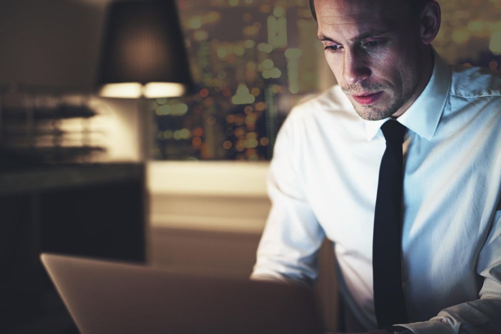 Focused man in shirt and tie working on his laptop at night