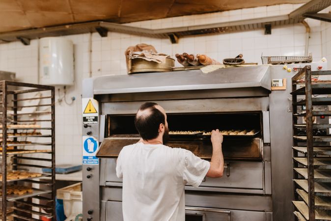 Bald baker checking pastry inside oven