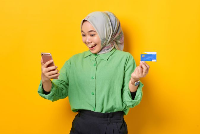 Happy Muslim woman in headscarf and green blouse receiving good news on her smart phone