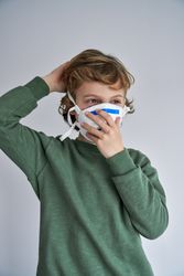 Boy putting on protective face mask and wearing green sweater