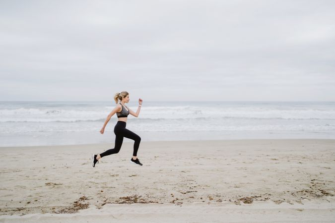 Young female athlete in active wear jogging while jumping at sea beach
