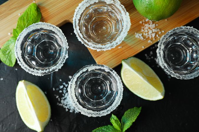 Tequila shots with salt, lime slices and mint on dark table