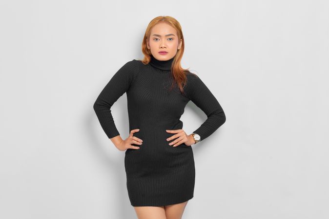 Asian woman looking at camera with hands on hips, red hair and turtle neck dress in studio