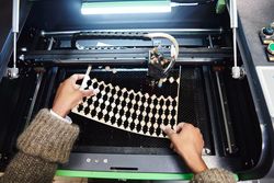 Close up hands removing pieces from a laser cutter