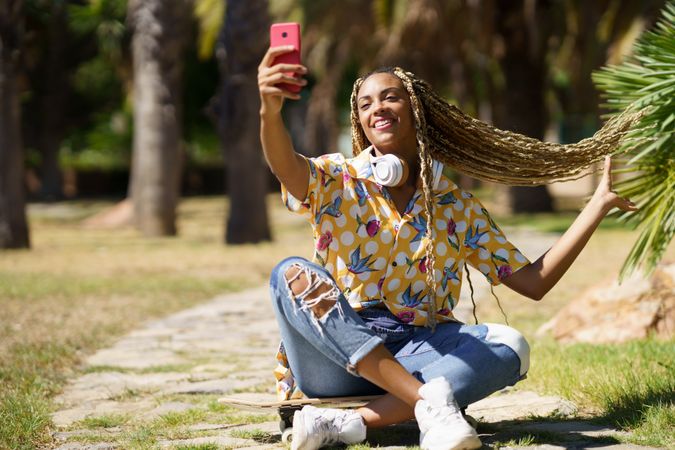 Female in bold patterned shirt taking selfie in park while holding up her braids