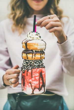 Woman holding stacked donut milkshake with straws, whipped cream, and chocolate sprinkles