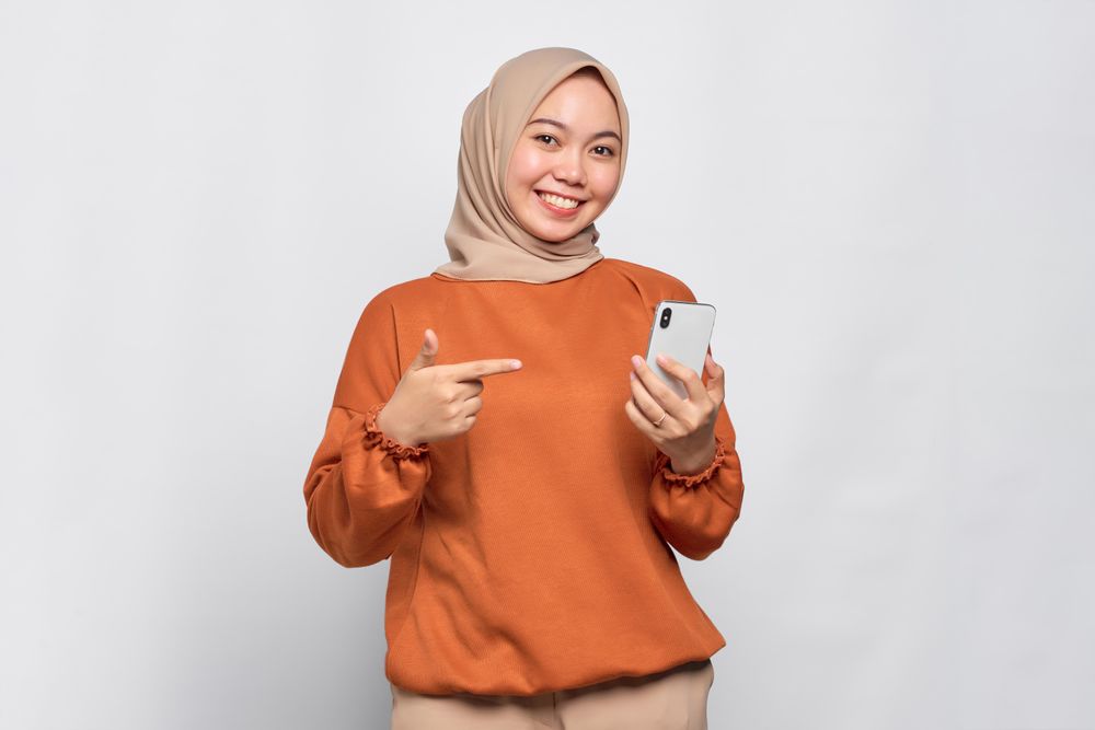 Cheerful Muslim woman pointing at her smartphone
