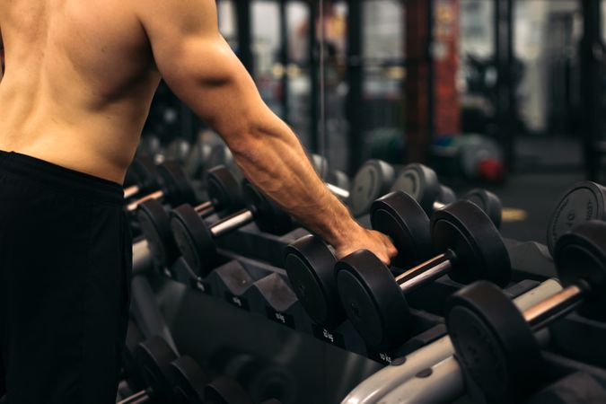 shirtless strong man lifting dumbbell in a gym