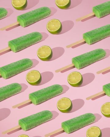 Rows of green ice pop and lime halves on pink background with shadow