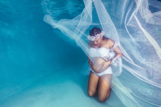 Pregnant woman in wreath and dress underwater