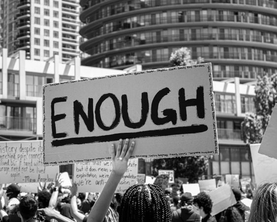 Grayscale photo of a banner with word " Enough" held at protest 