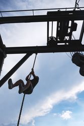 Anonymous man climbing rope in outdoor gym