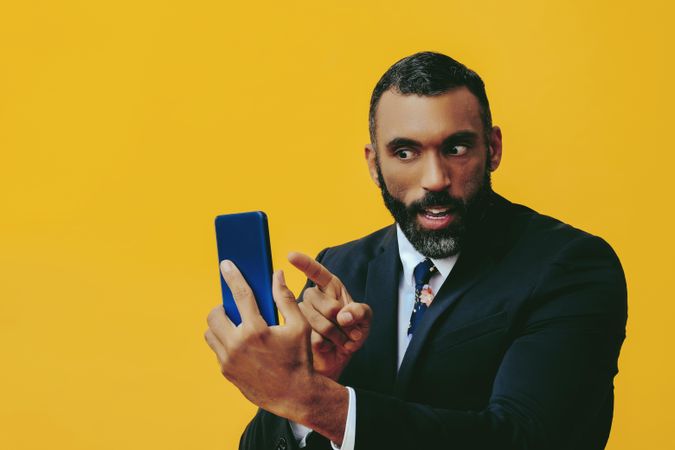 Intense Black businessman in suit speaking at smartphone screen while pointing