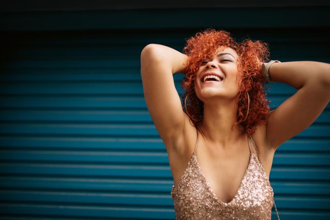 Woman in happy mood laughing with eyes closed holding her curly golden brown hair