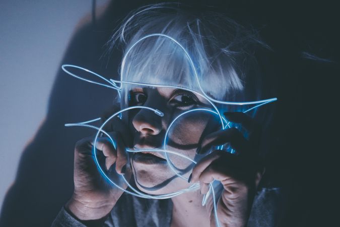 Portrait of neutral woman with light hair holding blue led light thread