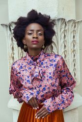 Woman in blue and pink floral top and brown skirt leaning on a wall