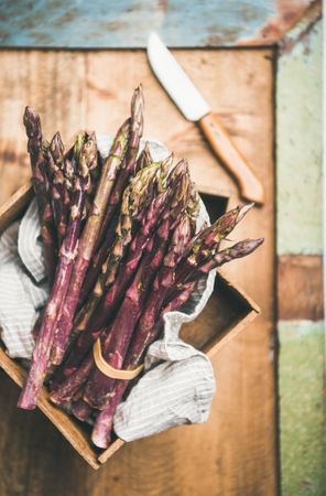 Close up of bunches of purple asparagus, knife on blue green background, vertical composition