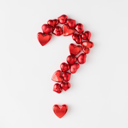 Question mark made of red foil hearts on light background