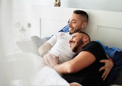 Smiling gay couple hugging on bed