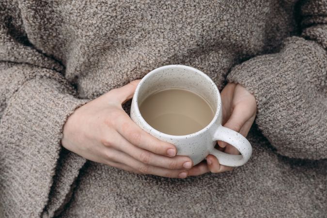 Female hands in beige pullover holding ceramic cup of coffee