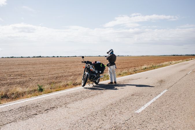 Man on side of a quiet rural road with motorcycle