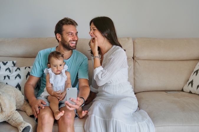 Cheerful family with baby using smartphones on sofa