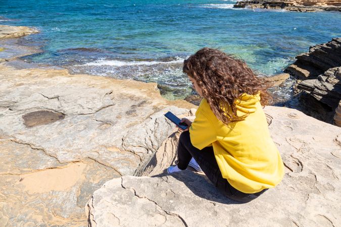 Young woman using mobile phone sitting near the beach