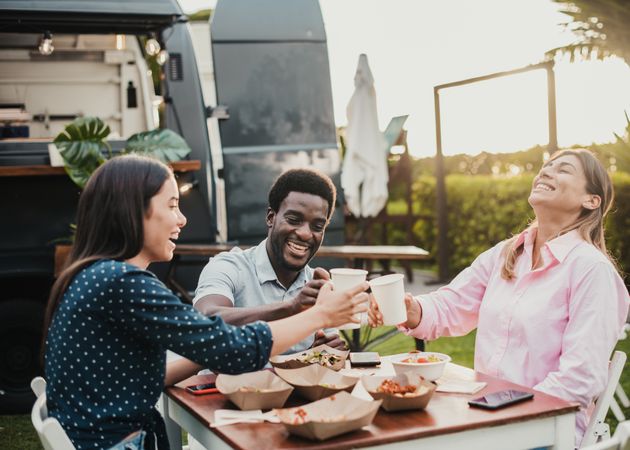 Happy people eating and cheering at food truck restaurant - Focus on african man face