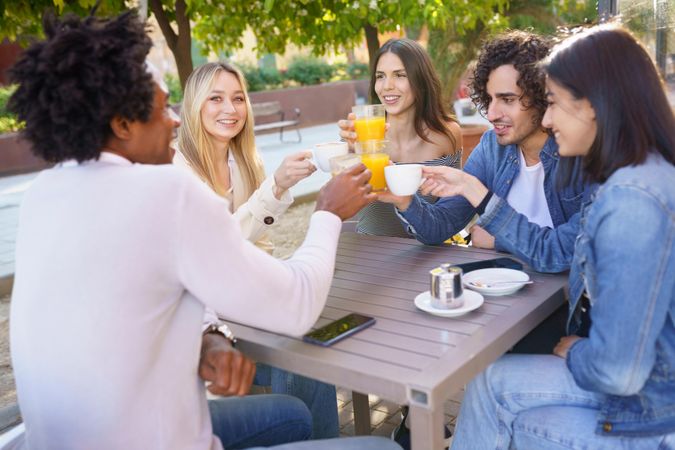 Multi-ethnic friends raising their juice and coffee in celebration at an outdoor restaurant