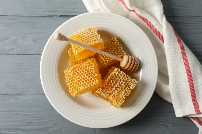 Plate with dipper and honeycombs on wooden background, space for text
