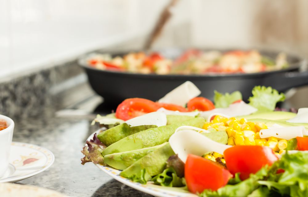 Closeup of fresh salad dish and female cooking in a pan