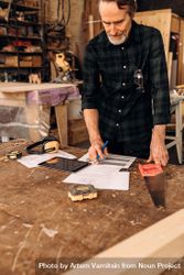 Older man with design plans in his woodwork shop, vertical 4ZD930