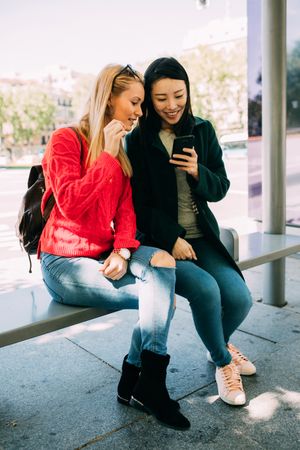 Female friends using smartphone on bus stop